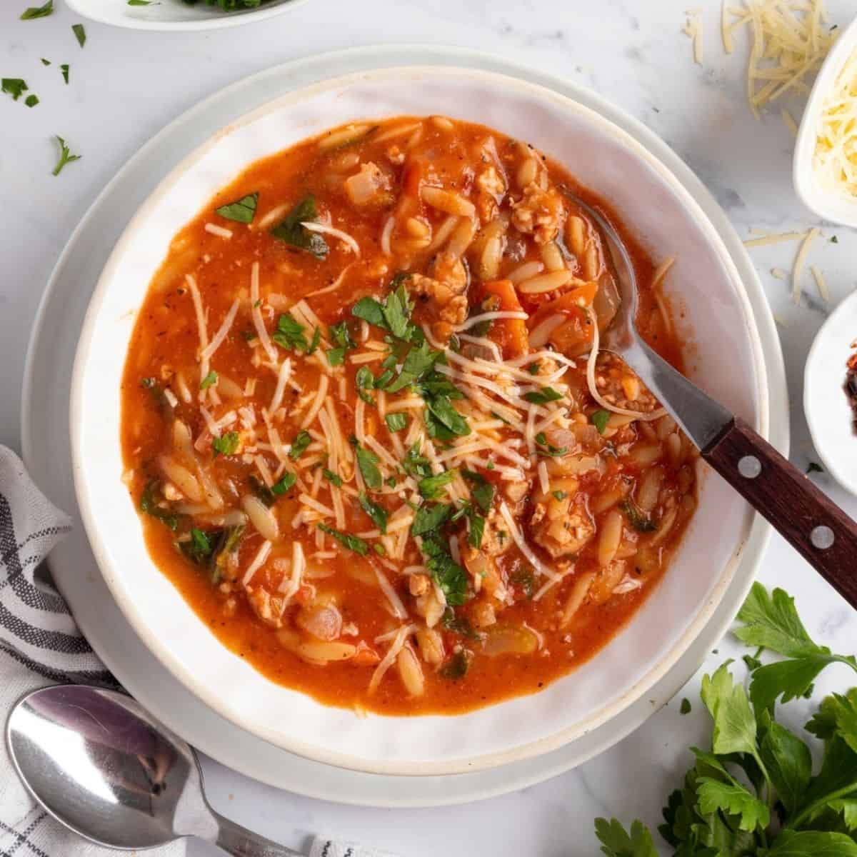 A bowl of sausage orzo soup with a spoon resting in the bowl.