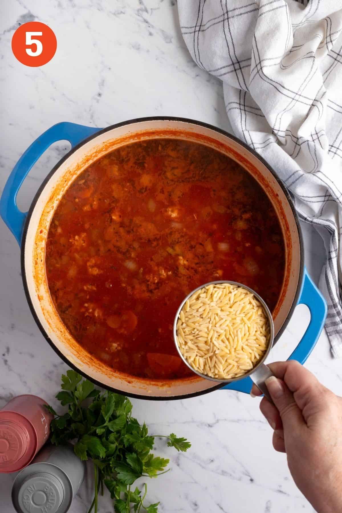 Adding orzo into the simmering sausage soup.